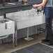 A man standing at a Regency stainless steel underbar drainboard with glasses on it.