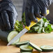 A person in black gloves using a Victorinox yellow serrated paring knife to cut a cucumber on a table.