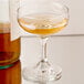 A Libbey Embassy coupe glass filled with a clear liquid next to a bottle.