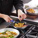 A chef using a Choice silicone pan handle cover on a pan of potatoes and vegetables on a stove.