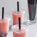 A group of plastic cups with pink drinks, each with a black pointed unwrapped straw in it.