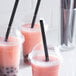 Three pink drinks in plastic cups with black pointed straws.