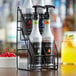 A Monin bottle of syrup sits in a Monin 2 tier bottle holder on a counter.