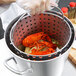 A person using a Vollrath Wear-Ever fryer basket to cook lobsters and corn.