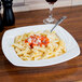 A plate of pasta with sauce in a CAC white square porcelain pasta bowl with a fork on the plate.