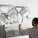 A man hanging pots and pans from a Regency stainless steel ceiling-mounted pot rack.
