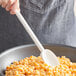 A Mercer Culinary white high temperature mixing spoon stirring macaroni in a pan.