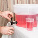 A hand pouring a pink drink from a tap into a Carlisle round plastic beverage dispenser.
