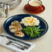 An Acopa Azora blue stoneware coupe plate with chicken, mashed potatoes, and green beans on a table with a cup of coffee.