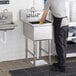 A man washing a Regency stainless steel commercial sink in a professional kitchen.