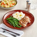 An Acopa Keystone Sedona Orange stoneware coupe plate with chicken, green beans, and rice on it.
