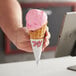 A hand holding a JOY small waffle cone with a scoop of pink ice cream