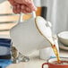 A person pouring tea into a white Acopa Keystone stoneware teapot.
