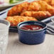 A blue Acopa stoneware ramekin filled with red sauce on a table with chicken nuggets.