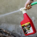 A person using Victor Pest Snake-A-Way hose end snake repellent to spray a red liquid into a pile of dirt.