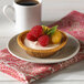 A Keebler graham tart shell filled with raspberries and cream on a plate with a mint garnish next to a cup of coffee.