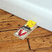 A Victor Pest wood mouse trap with a yellow and black metal spring on a wooden floor.