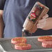A person pouring McCormick Grill Mates Hamburger Seasoning onto burgers.