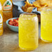 A glass of yellow Jarritos Passion Fruit soda on a table with chips and salsa.