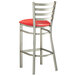 A Lancaster Table & Seating metal bar stool with a red vinyl padded seat.