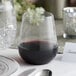 A Visions clear plastic stemless wine glass filled with red wine on a table.