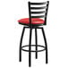 A Lancaster Table & Seating black finish ladder back swivel bar stool with red vinyl padded seat.