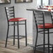 A Lancaster Table & Seating black ladder back bar stool with a burgundy cushion on the seat.