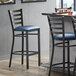 A Lancaster Table & Seating ladder back bar stool with a navy blue cushion on the seat.