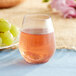 A clear plastic stemless wine sampler glass filled with wine on a table next to grapes.