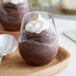 A clear plastic stemless wine sampler glass filled with chocolate pudding and whipped cream.