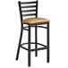 A black Lancaster Table & Seating ladder back bar stool with a light brown vinyl seat.