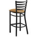 A Lancaster Table & Seating black ladder back bar stool with a light brown cushion.