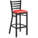 A black Lancaster Table & Seating ladder back bar stool with a red vinyl padded seat.