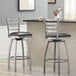 Two Lancaster Table & Seating silver bar stools with black vinyl padded seats at a counter.
