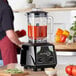 A AvaMix commercial blender with red liquid and vegetables in it on a kitchen counter.