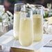 Three Visions clear plastic stemless champagne flutes with gold rims filled with champagne on a white surface.