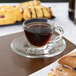 A Libbey espresso saucer with a glass cup of coffee on a table with pastries.