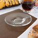 A hand holding a Libbey glass cup of espresso on a saucer with pastries on a table.