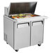 A Turbo Air stainless steel 2 door refrigerated sandwich prep table on a counter with food trays.
