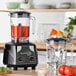A AvaMix commercial blender with red liquid inside and a tomato on top.