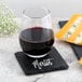 A glass of red wine on a black slate coaster with cheese on it.
