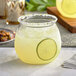 A Visions clear plastic stemless fish bowl glass with a drink and a lime slice in it on a white table with a stack of folded white napkins.