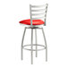 A Lancaster Table & Seating clear coat finish ladder back swivel bar stool with a red vinyl padded seat.
