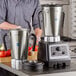 A man in a grey shirt using a silver AvaMix commercial food blender.