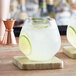 Two Visions clear plastic stemless wine glasses filled with limeade on a wooden coaster.