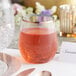 A Visions stemless wine glass with rose gold rim filled with red liquid on a table.