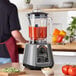 An AvaMix commercial blender with a red liquid in it on a counter.