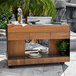 An Indu+ outdoor mobile bistro island with a wood counter and a barbecue grill on a stone surface.