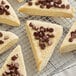 A group of triangle-shaped scones with Guittard semi-sweet chocolate chips on a cooling rack.