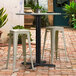 A Lancaster Table & Seating black table base with white stools on a brick patio.